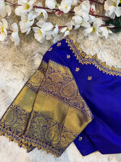A close-up of the sleeve of a royal blue blouse, showing the rich gold zari work that is characteristic of Kanjeevaram sarees.