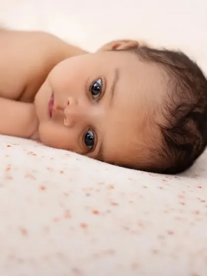 A simple, beautiful portrait of a newborn lying on a speckled blanket. This minimalist shot focuses entirely on the baby's delicate features and soulful eyes.