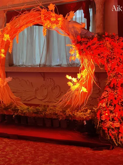 A unique and artistic circular arch made of twigs and branches, glowing with fiery red light and flowers. This makes for a dramatic and unforgettable photo backdrop or entrance piece.