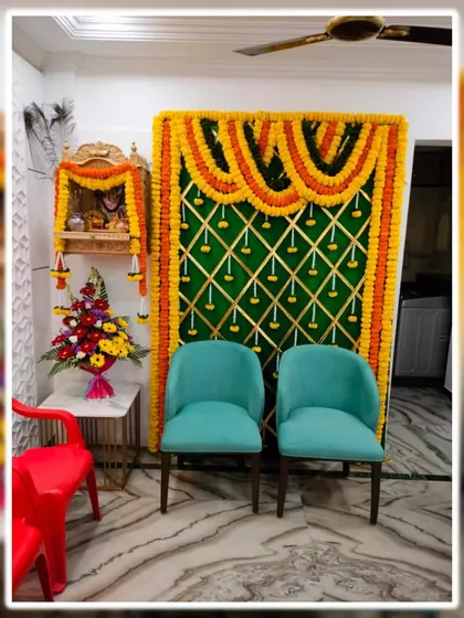 This is a budget friendly decoration we did for a home pooja. It features a traditional marigold backdrop next to the home mandir, with chairs for seating, creating a functional and festive corner.