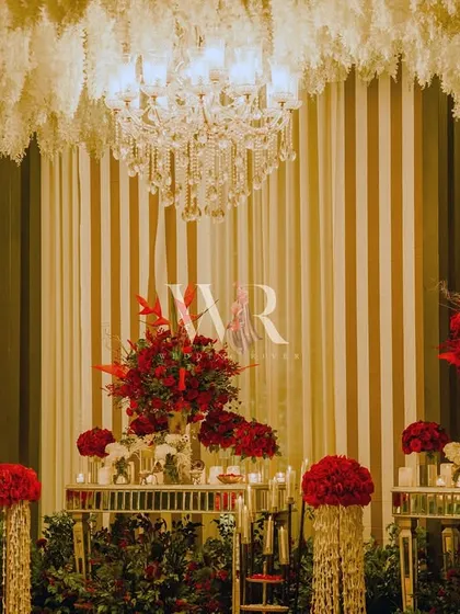 A symphony of red and white. This installation features mirrored tables topped with dramatic red floral arrangements, set against a backdrop of white and gold stripes and a ceiling of hanging white flowers.