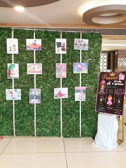 For a personal touch, I created this milestone photo wall against a boxwood greenery panel. It displays photos from the baby's first year, alongside a custom board detailing her milestones, making for a sentimental and engaging feature for guests.