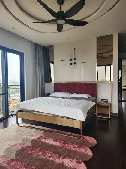 The master bedroom in the Quintessence project, featuring a custom brass-framed bed with a rich red velvet headboard. Mirrored panels behind the bed enhance the sense of space and reflect the lake views from the large windows, creating a luxurious and serene retreat.