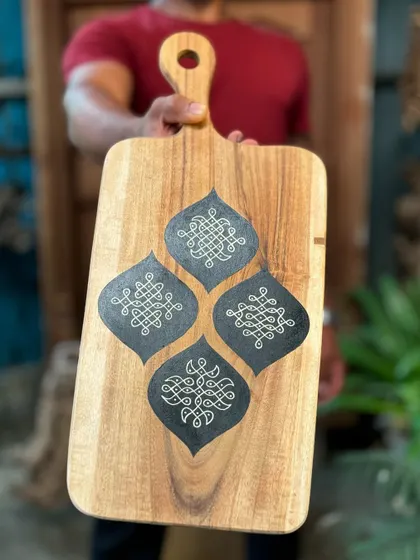 A hand-painted wooden platter with traditional rangoli designs. These organically shaped pieces are perfect for festive decor, whether you hang them on a wall or use them as a serving platter.