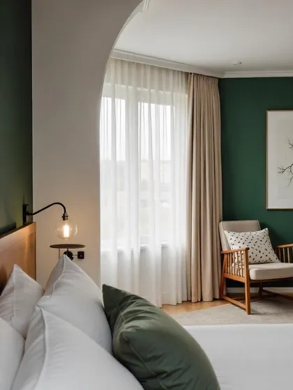 A beautiful space with a mix of cool and warm tones. The deep green accent wall is softened by the arched entryway and sheer curtains, creating a cozy and elegant reading nook next to the bed.