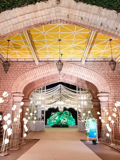 A whimsical pathway lined with glowing tulip-shaped lights leads guests through a brick archway into the main event space.
