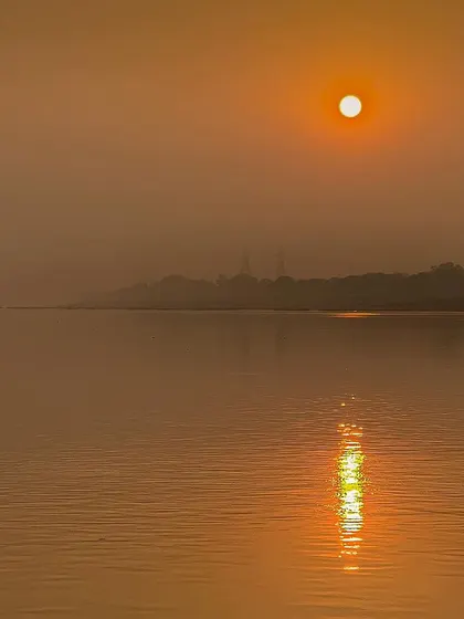 A minimalist photograph of the sun hanging over a calm body of water in the morning haze. The reflection on the water adds a touch of life to the serene scene.