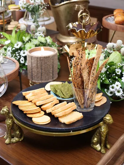 The black marble cheetah-footed stand, styled with crackers and a candle. This versatile piece can be used for serving both sweet and savory treats, adding character to any spread.