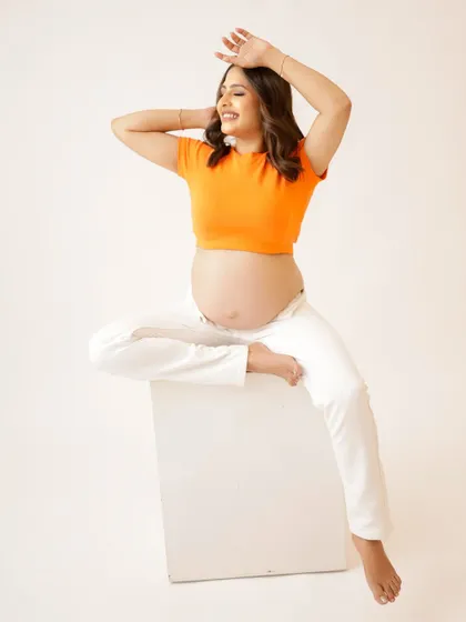 A joyful and energetic portrait. The mom-to-be is all smiles in a casual, stylish outfit, her pose full of confidence and happiness.
