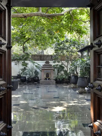 The entrance to the Courtyard Home is a narrative of heritage and tranquility. Framed by old Chettinad doors and teak columns from Kerala, the view opens to a courtyard centered around a temple replica, immediately grounding the home in a rich, cultural context and a sense of peace.