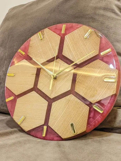 The honeycomb wood and resin clock resting on a couch, showcasing its unique design and color. The pink resin adds a pop of color while the wood keeps it grounded and warm.