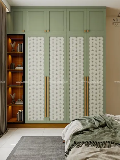 A beautiful wardrobe design featuring sage green doors with patterned fabric panels. The open shelving on the side provides a perfect spot for books and decor.