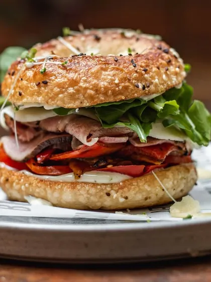 A fully loaded everything bagel sandwich. We stack it high with meats, cheeses, and fresh arugula for a satisfying and delicious meal.