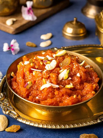 A comforting bowl of Gajar Halwa, a classic winter dessert, presented in a brass bowl against a deep blue background.