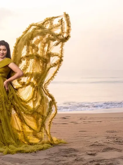 The flowing yellow gown creates a beautiful, dynamic shape against the sea, a perfect portrait of a glowing mother-to-be.