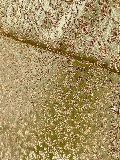 A detailed view of a gold and green brocade fabric, showcasing the intricate texture and sheen that makes it perfect for high-end festive garments.