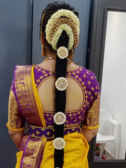 A back view showcasing the traditional poola jada, or flower braid. This classic South Indian bridal hairstyle uses fresh flowers and hair ornaments to create a long, decorated braid that complements the silk saree.