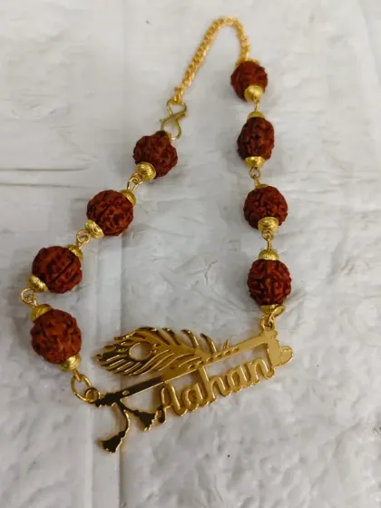 A personalized rakhi bracelet featuring a name cut-out with a peacock feather design, paired with rudraksh beads.