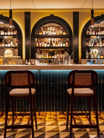 A direct, eye-level shot of the bar at Vamos Experience. I focused on the intricate tilework, the classic design of the bar stools, and the beautifully lit bottle display to create a clean and inviting image of the bar area.