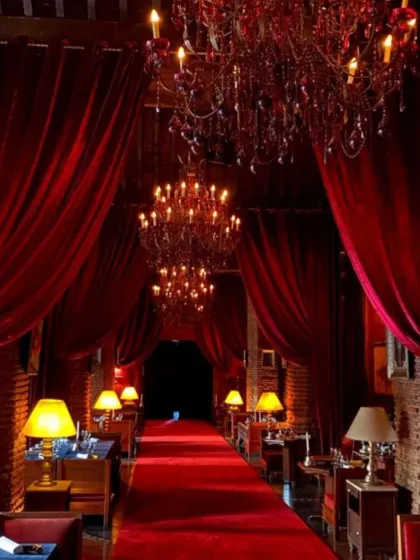 This entrance evokes the glamour of an old-world theatre or a luxurious lounge. Rich red velvet curtains and a red carpet are complemented by warm table lamps and crystal chandeliers, creating a dramatic and opulent welcome.