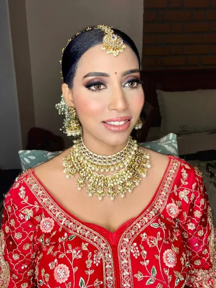 A classic red bridal look with a sleek bun and gajra. The makeup is timeless, with defined eyes and a lip color that complements her golden jewelry.