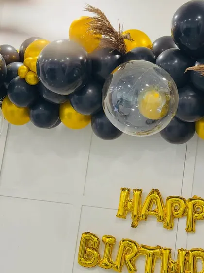 A close-up view of the black and gold balloon decor, showing the mix of textures with clear confetti balloons and dried pampas grass for a modern, chic look.