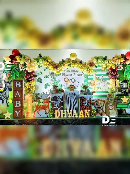 A full stage view of Dhyaan's jungle-themed first birthday, showcasing a vibrant balloon arch, animal cutouts, and personalized name display.