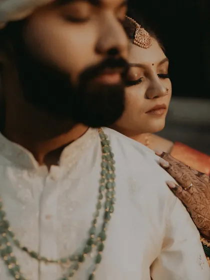 A moody and intimate close-up portrait of the couple, highlighting the texture of their attire and the groom's emerald necklace.