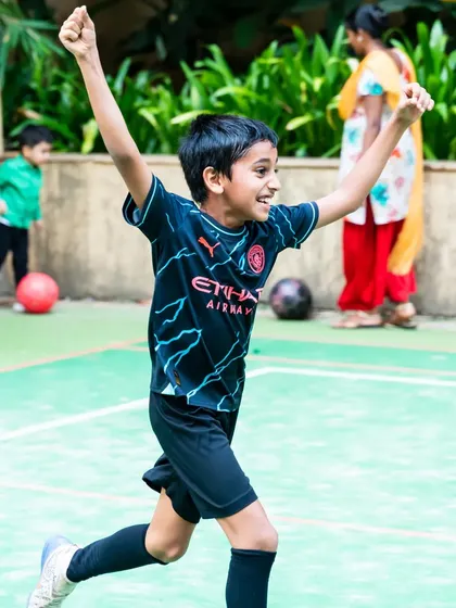An action shot of the birthday boy celebrating a goal with his arms raised in victory during his football party.