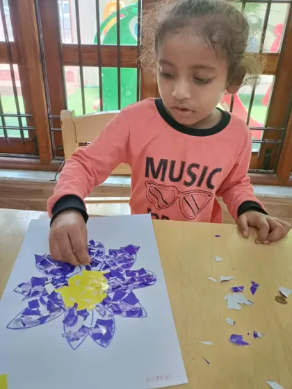 This little artist is focused on filling in her flower design with torn purple paper. This collage technique is a great way to explore texture and color.