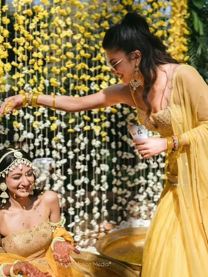 A candid moment from a Haldi ceremony, with the bride being showered with petals against a backdrop of cascading yellow and white flower strings.