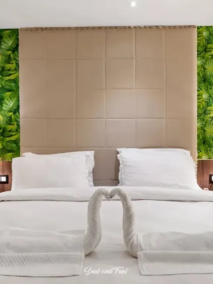 A close-up of the bed in the hotel room, with towels folded into swan shapes. The green accent wall and warm bedside lamps create a tropical and inviting atmosphere.