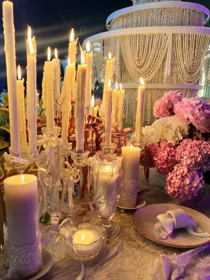A sea of candles in crystal holders casts a warm, romantic glow over the 'Lace Love' tablescape. The flickering light highlights the delicate textures of the lace and the soft petals of the flowers.