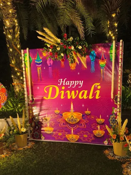 A custom 'Happy Diwali' printed backdrop for an outdoor party, flanked by floral arrangements.