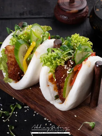 These bao buns are styled on a dark wooden board to make their soft, white texture stand out. The vibrant green fillings add a fresh contrast, making the dish look light and flavorful.
