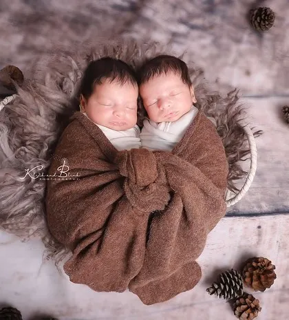 Two peas in a pod. The twins are swaddled together in a single brown wrap, creating a heart shape that perfectly symbolizes their bond.