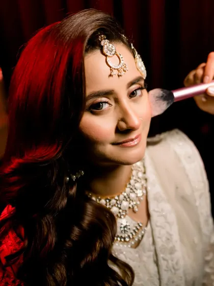 A close-up shot of the bride getting her makeup touched up. Her direct gaze into the camera is confident and beautiful, capturing a behind-the-scenes moment with style.