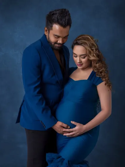 A tender moment where the couple looks down at the baby bump together. Their coordinated blue outfits and the artistic backdrop create a cohesive and beautifully styled maternity photo.