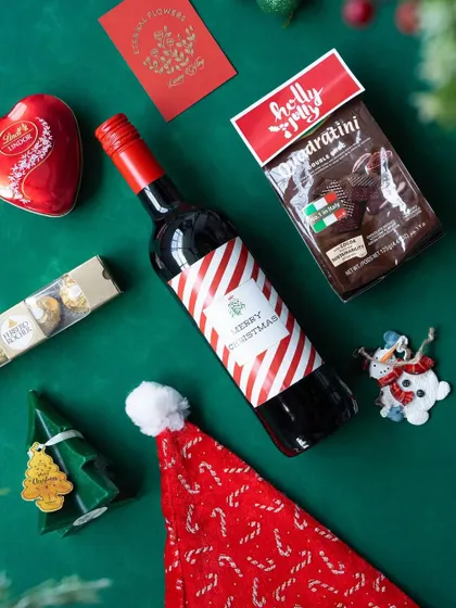 A flat lay of the 'Jolly Feast' hamper contents, including a Santa hat, wine, chocolates, and a tree-shaped candle.