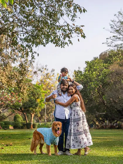 A happy family portrait in the park, with the dad holding his son on his shoulders while their Golden Retriever stands proudly.