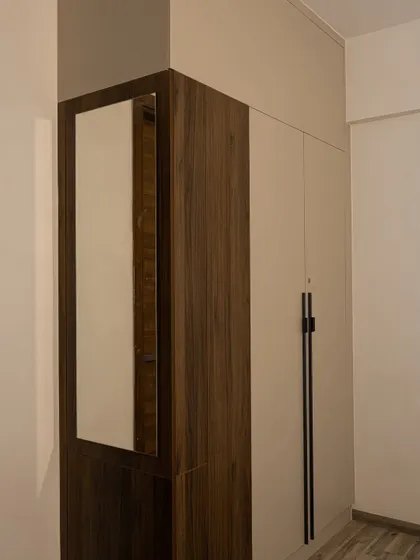 A space-saving corner wardrobe unit with an integrated mirror. The dual-tone design with wood grain and off-white laminate is both modern and practical for smaller rooms.