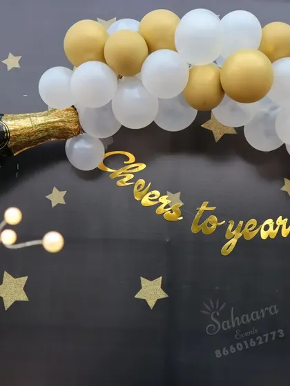 "Cheers to the years!" This fun bachelor party or milestone birthday backdrop features a champagne bottle balloon, a starry night theme, and a table for cake and gifts.
