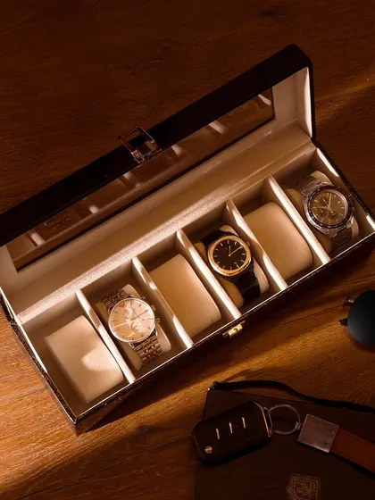 An overhead shot of a watch collection box on a wooden surface. The play of light and shadow adds a dramatic, premium feel, perfect for luxury accessory brands.