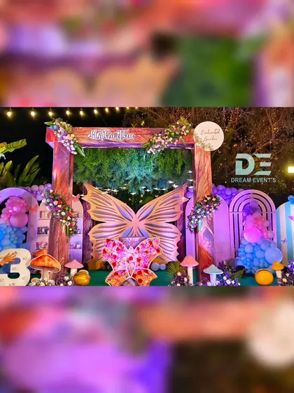 An outdoor enchanted garden party at dusk, with purple lighting creating a magical ambiance around the butterfly-themed stage.