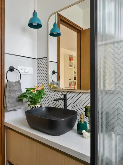A powder room with a black vessel sink, geometric-patterned tiles, and vibrant teal pendant lights that add a pop of color.