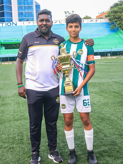 Guided to victory. A young team captain stands proudly with his coach and the championship trophy, representing the leadership and development we foster.
