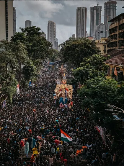 A drone's view of the procession snaking through the city, with modern skyscrapers in the background, creating a contrast between tradition and urban life.