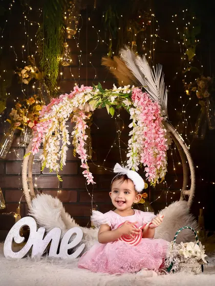 A beautiful first birthday portrait with a stunning floral and fairy light backdrop. The pink dress and sweet lollipop complete this magical scene.
