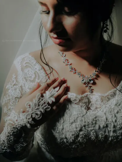 A close up portrait focusing on the delicate lace of the bride's dress and her sparkling necklace.