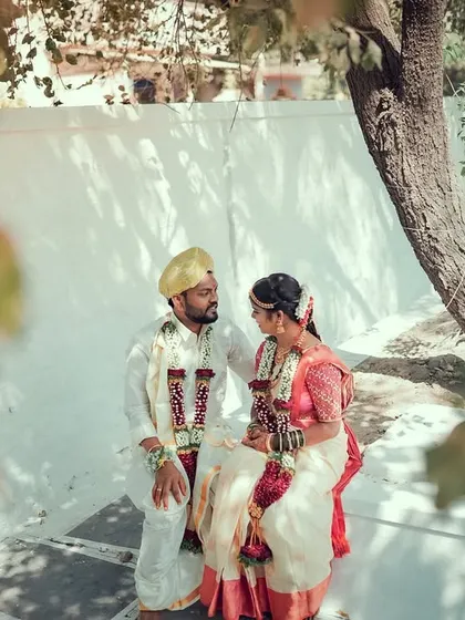A quiet moment shared between a newly married couple under a tree, away from the wedding hustle.